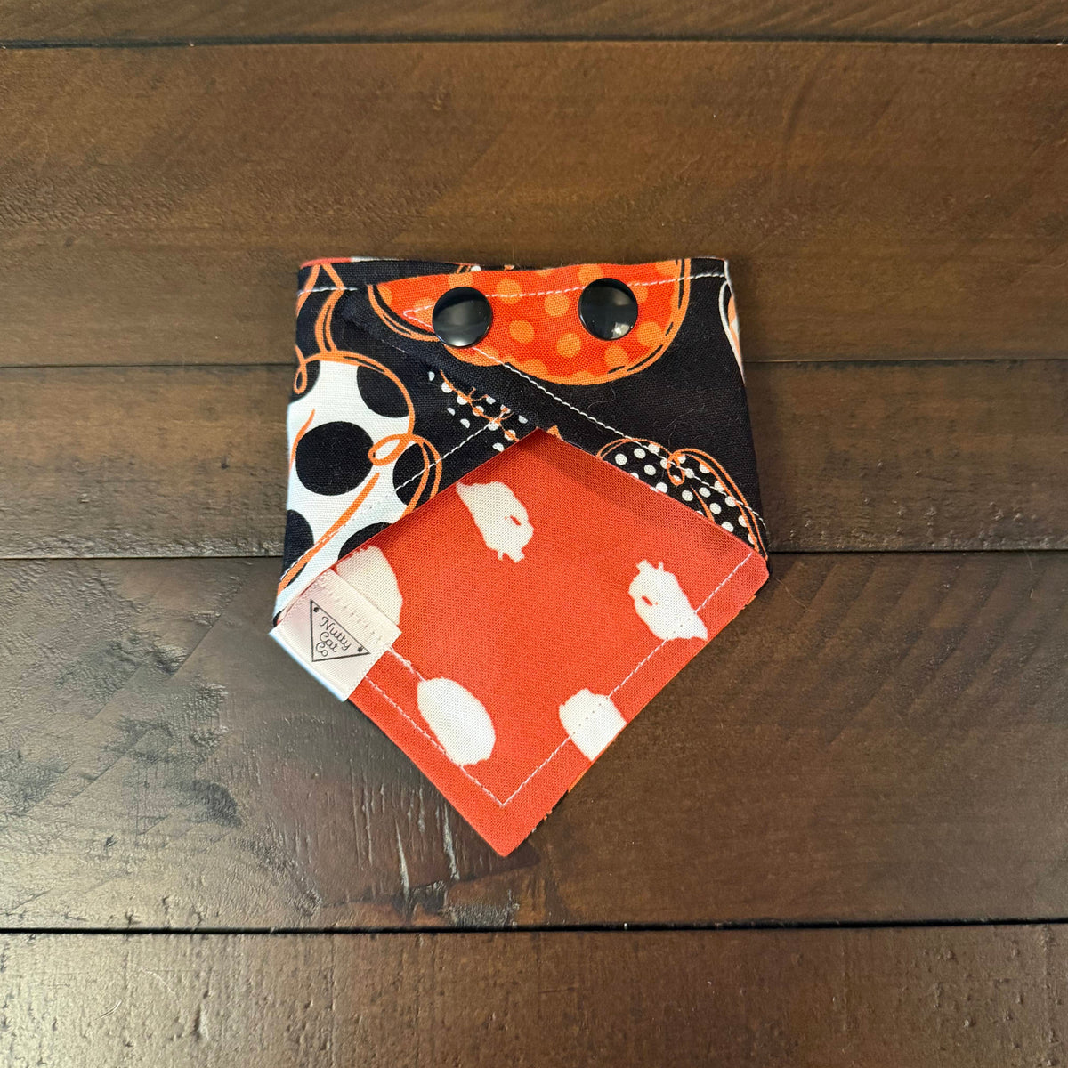 Pumpkin Mashup pet bandana showing an orange reverse with white polka dots and black snaps.