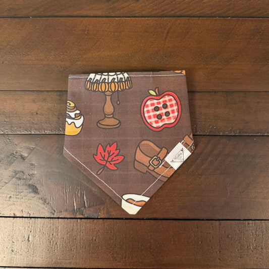 Dark chocolate brown pet bandana with an apple button, autumn leaf, lamp, shoe, and iced cinnamon roll.