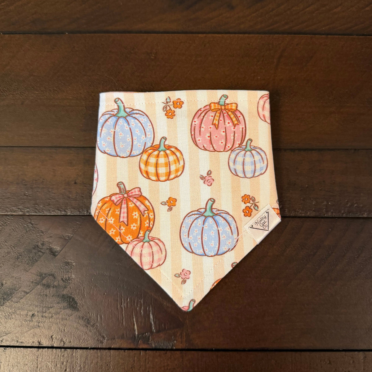 Cream and tan striped pet bandana with pink, blue, and orange pumpkins, ribbon bows, and small flowers.