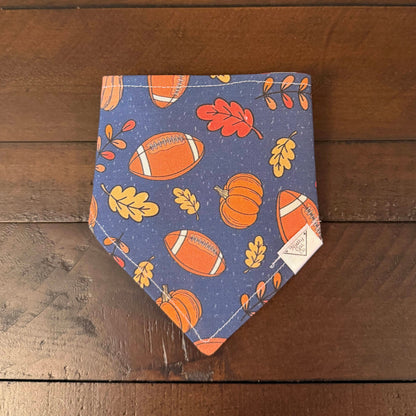 Blue pet bandana with footballs, orange pumpkins, and red and yellow autumn leaves.