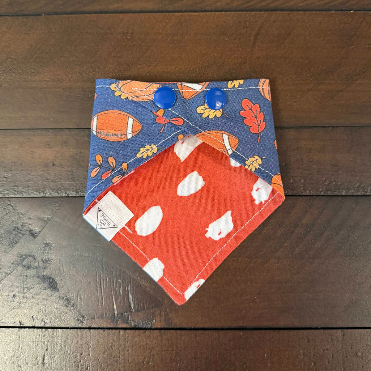 The Furry MVP Football pet bandana showing an orange reverse with white polka dots and blue snaps.
