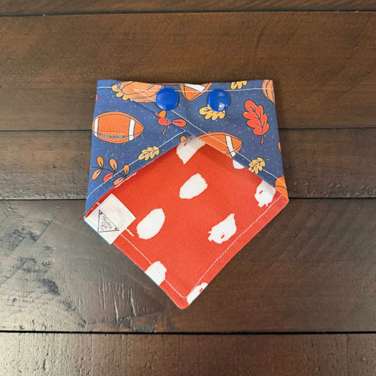 Blue pet bandana with footballs, orange pumpkins, and red and yellow autumn leaves.