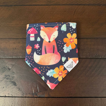 Navy pet bandana with an orange fox, colorful flowers, mushrooms, acorns, and leaves.