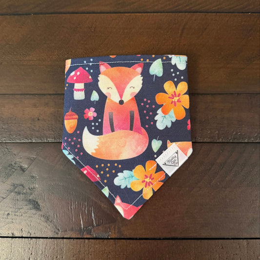 Navy pet bandana with an orange fox, colorful flowers, mushrooms, acorns, and leaves.