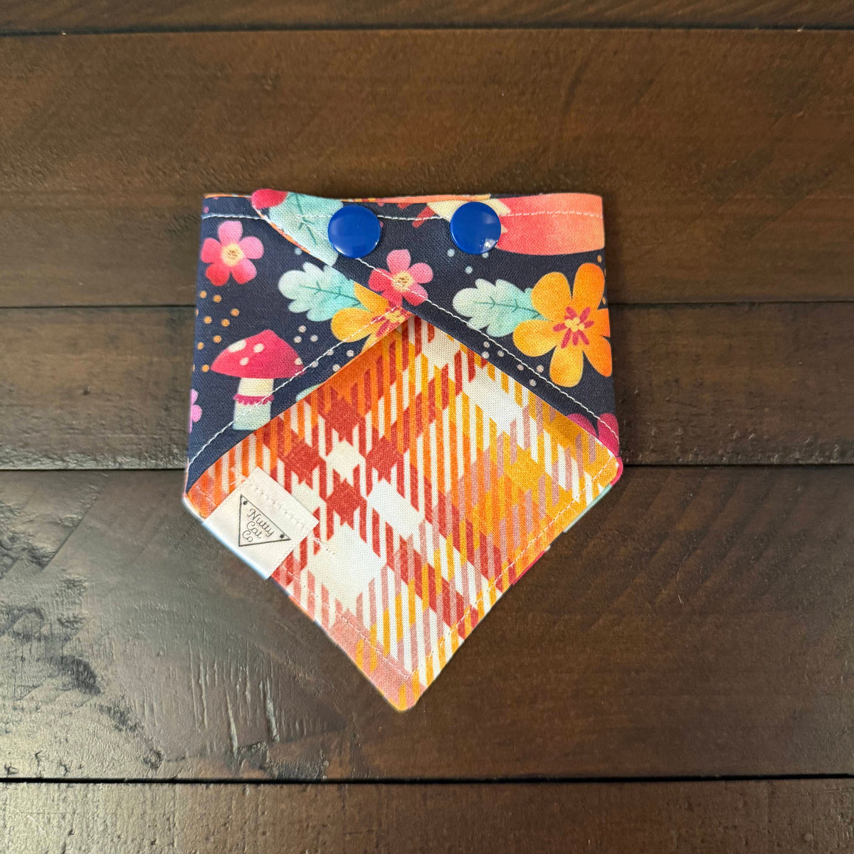 Foxy Fall Vibes pet bandana showing an orange, pink, and cream plaid reverse and dark blue snaps.