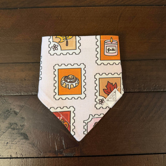 Pale pink pet bandana with postage stamp-style illustrations of autumn treats, a candle, and leaves.