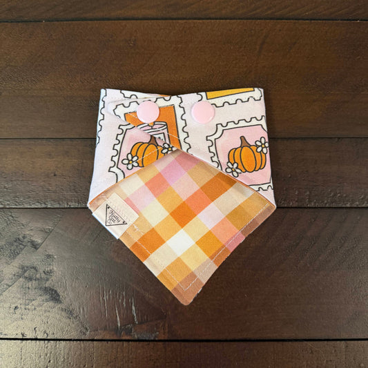 Pale pink pet bandana with postage stamp-style illustrations of autumn treats, a candle, and leaves.