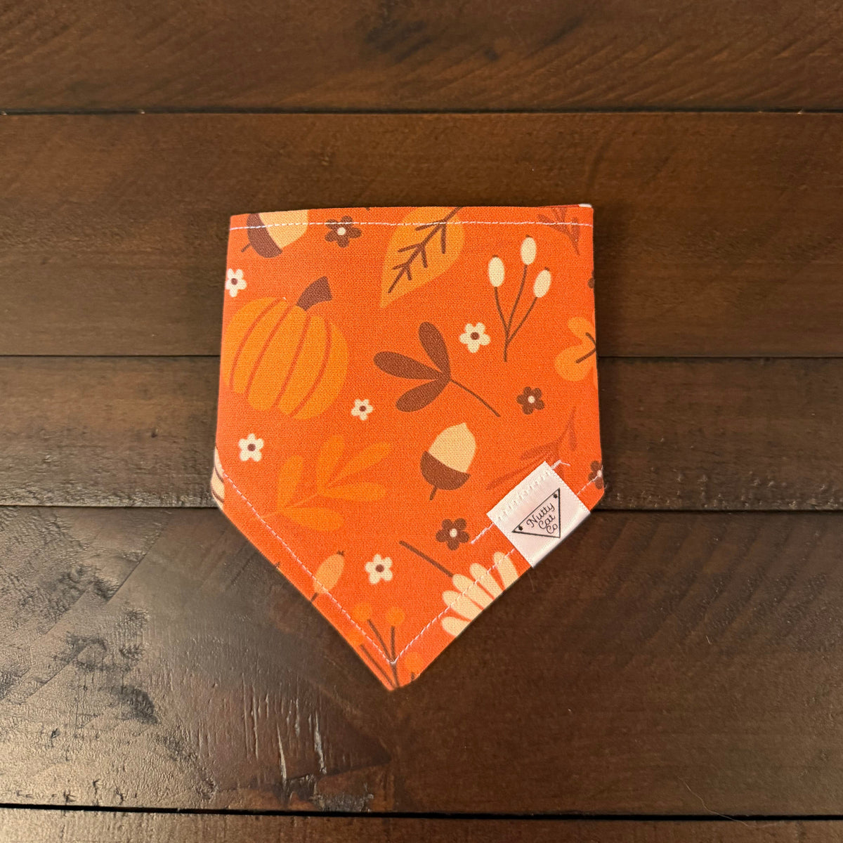 Orange pet bandana with pumpkins, acorns, leaves, branches, and small cream flowers.
