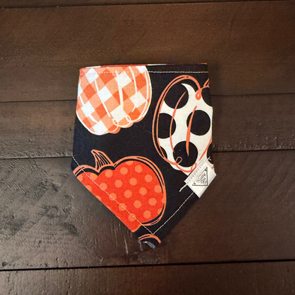 Black pet bandana with large orange and cream pumpkins decorated with checks and polka dots.