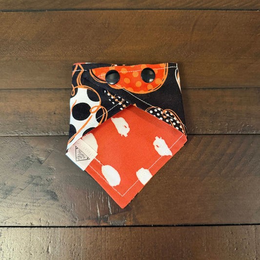 Black pet bandana with large orange and cream pumpkins decorated with checks and polka dots.
