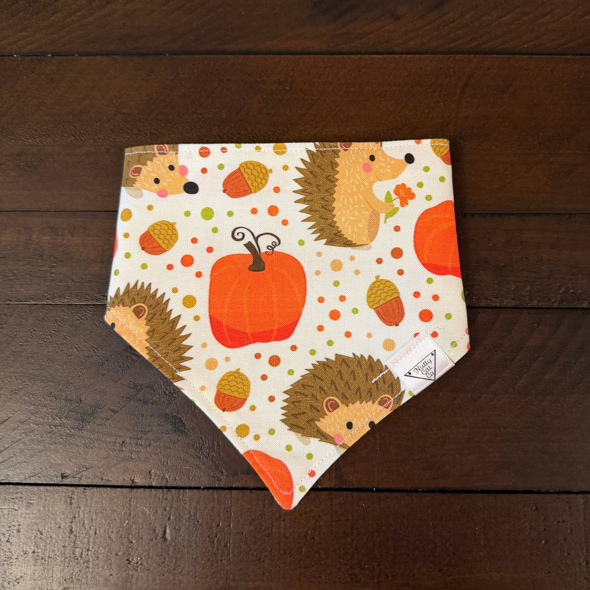 Cream pet bandana with hedgehogs, orange pumpkins, acorns, and colorful dots.